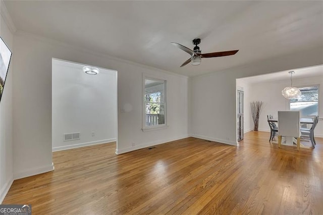 unfurnished living room with ceiling fan with notable chandelier, light hardwood / wood-style flooring, and crown molding