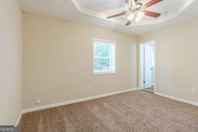 unfurnished room with a tray ceiling, ceiling fan, and carpet flooring