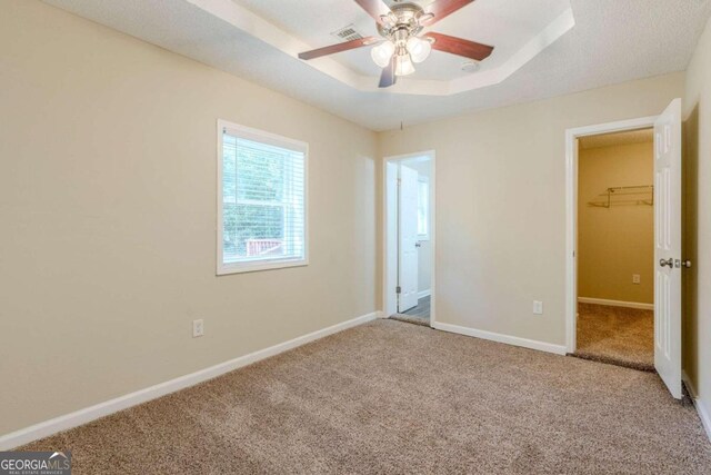 unfurnished bedroom featuring a spacious closet, ceiling fan, a raised ceiling, a closet, and carpet