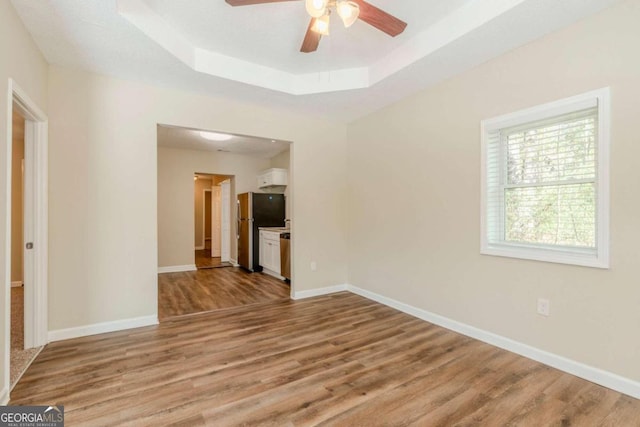 empty room with ceiling fan, light hardwood / wood-style floors, and a tray ceiling