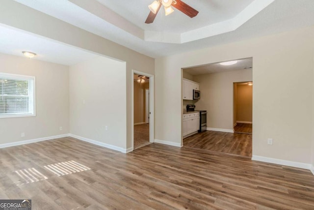 unfurnished living room with a tray ceiling, ceiling fan, and light hardwood / wood-style floors