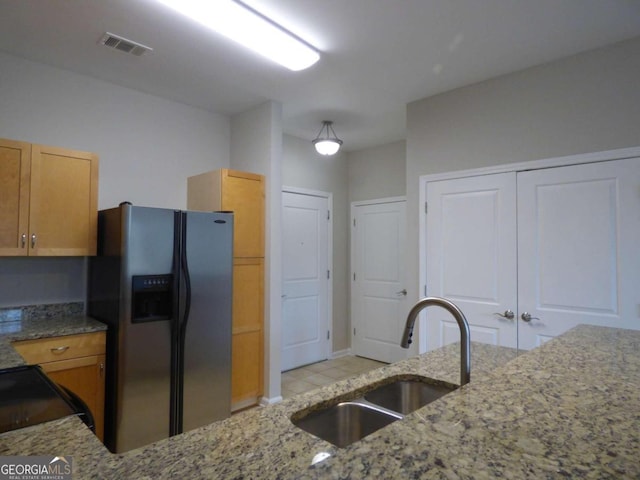 kitchen featuring black range oven, sink, stainless steel fridge, stone countertops, and light tile patterned flooring