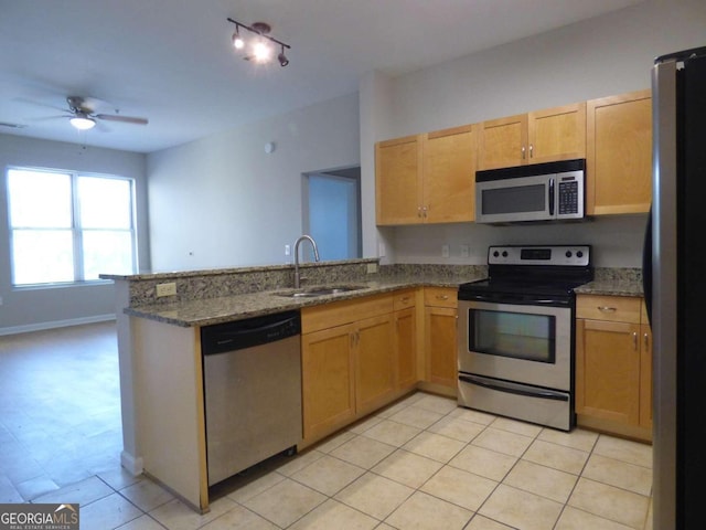 kitchen featuring kitchen peninsula, stainless steel appliances, ceiling fan, sink, and dark stone countertops