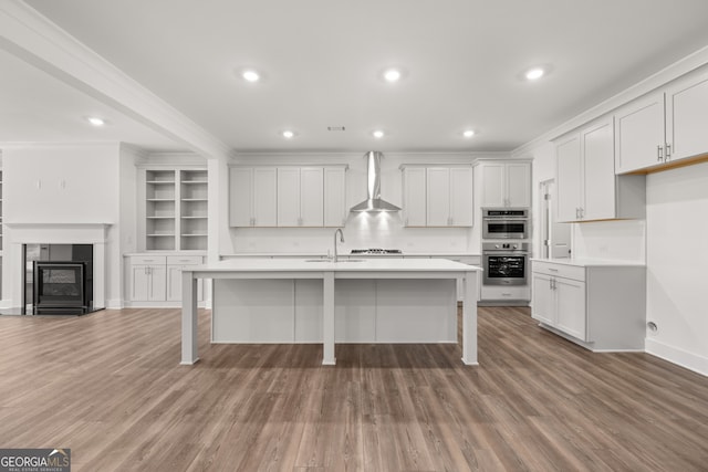 kitchen with a center island with sink, wall chimney exhaust hood, white cabinetry, and ornamental molding