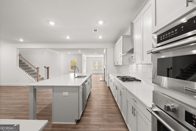 kitchen with appliances with stainless steel finishes, a kitchen breakfast bar, a kitchen island with sink, sink, and white cabinets