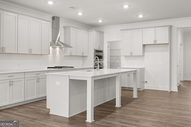 kitchen featuring dark hardwood / wood-style flooring, tasteful backsplash, a kitchen island with sink, sink, and wall chimney range hood