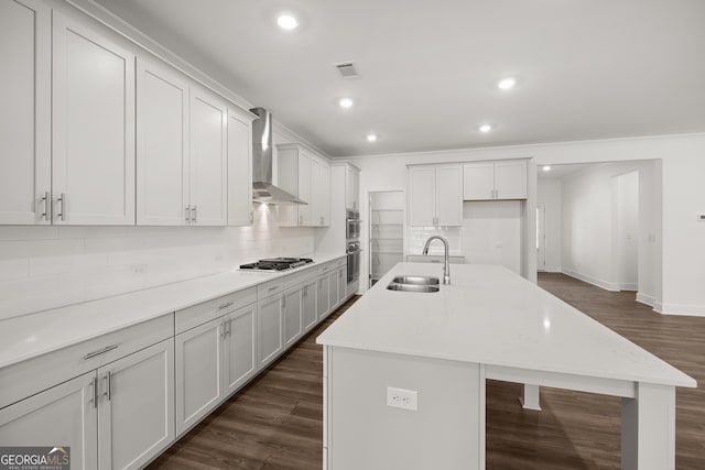 kitchen featuring white cabinets, sink, wall chimney exhaust hood, decorative backsplash, and an island with sink