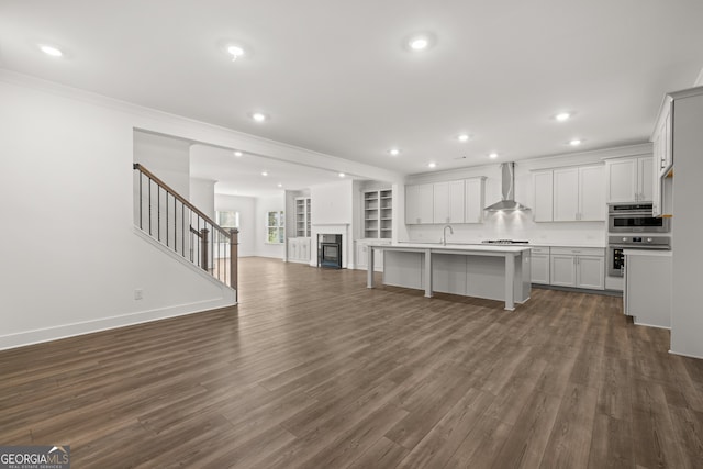 kitchen with wall chimney exhaust hood, ornamental molding, an island with sink, dark hardwood / wood-style flooring, and a breakfast bar area