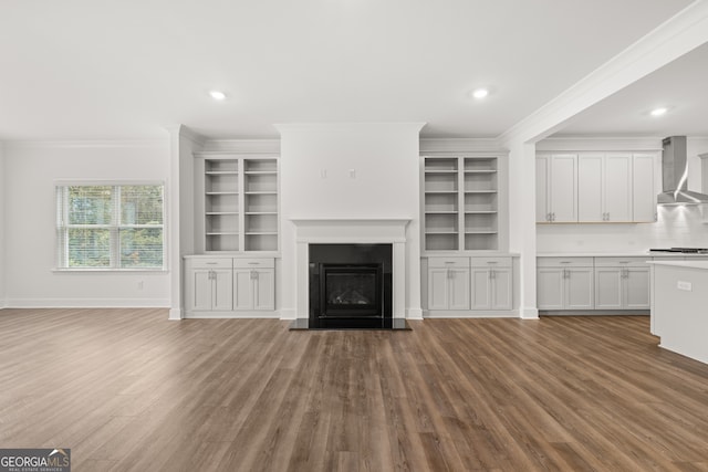 unfurnished living room featuring hardwood / wood-style flooring, built in features, and crown molding