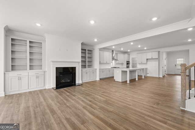 unfurnished living room featuring a fireplace, light wood-type flooring, built in features, and crown molding