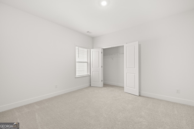 unfurnished bedroom with light colored carpet and a closet