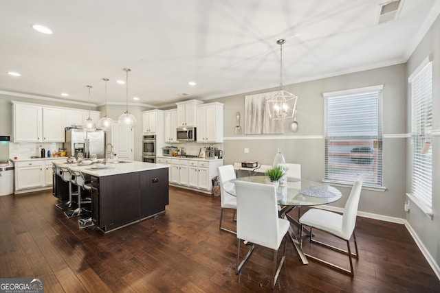 kitchen with white cabinetry, stainless steel appliances, an island with sink, pendant lighting, and a breakfast bar area