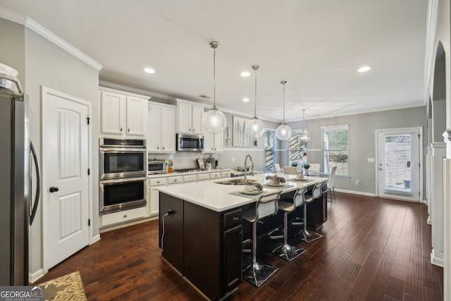 kitchen with dark hardwood / wood-style flooring, a breakfast bar area, a center island with sink, white cabinets, and appliances with stainless steel finishes