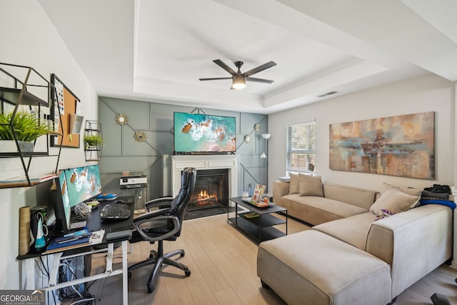 office area featuring light wood-type flooring, a tray ceiling, and ceiling fan