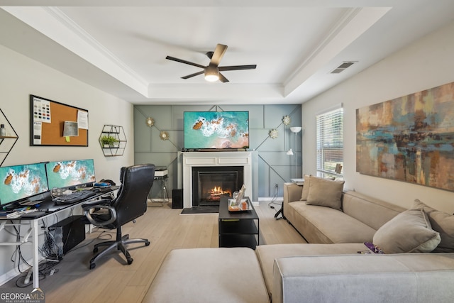 office space with ceiling fan, a raised ceiling, light wood-type flooring, and crown molding