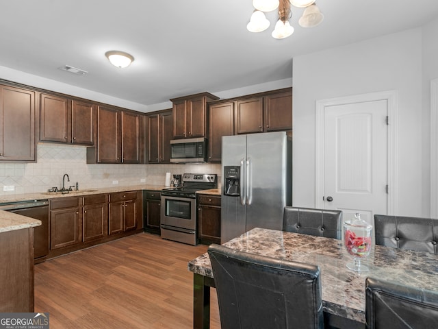 kitchen with hardwood / wood-style flooring, decorative backsplash, light stone countertops, dark brown cabinetry, and stainless steel appliances