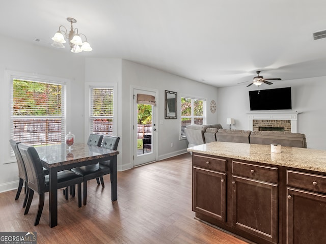 kitchen with light stone countertops, dark brown cabinetry, ceiling fan with notable chandelier, hardwood / wood-style flooring, and hanging light fixtures