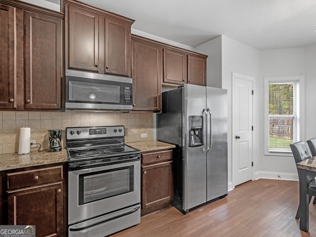 kitchen featuring light stone countertops, appliances with stainless steel finishes, tasteful backsplash, and light hardwood / wood-style flooring