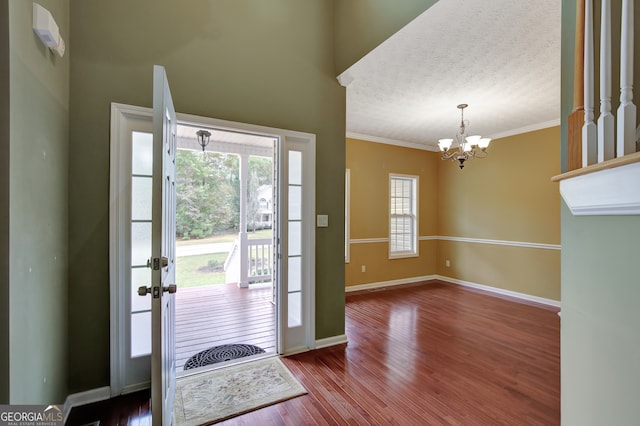 foyer entrance with a textured ceiling, hardwood / wood-style flooring, crown molding, and a notable chandelier