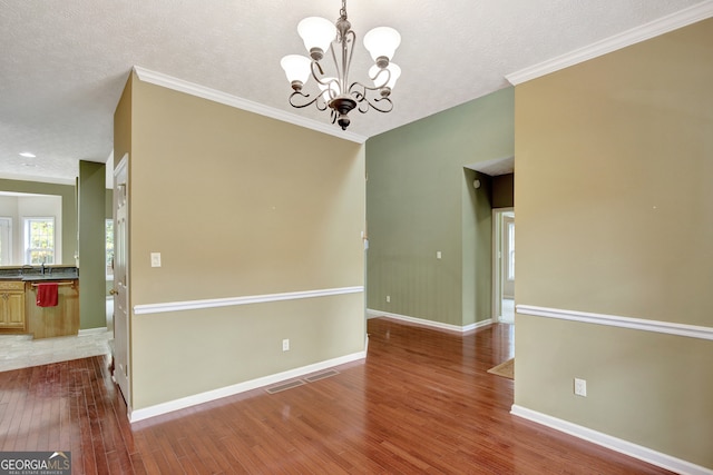 spare room featuring crown molding, hardwood / wood-style floors, a textured ceiling, and a notable chandelier