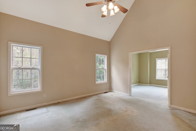 spare room with a healthy amount of sunlight, light carpet, and high vaulted ceiling