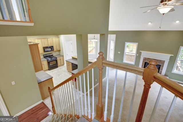 stairs featuring a stone fireplace, high vaulted ceiling, ceiling fan with notable chandelier, and hardwood / wood-style flooring