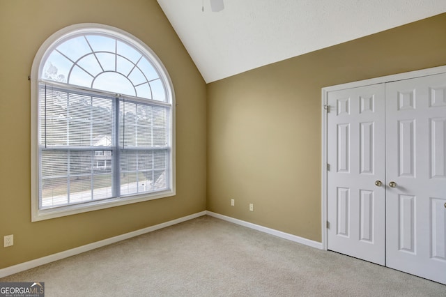 unfurnished bedroom featuring light carpet, a closet, lofted ceiling, and ceiling fan