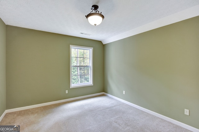 empty room featuring lofted ceiling, a textured ceiling, and light carpet