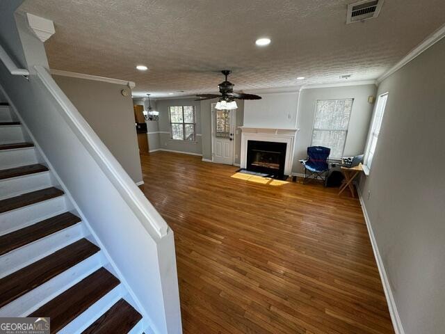 unfurnished living room with crown molding, hardwood / wood-style floors, ceiling fan, and a textured ceiling