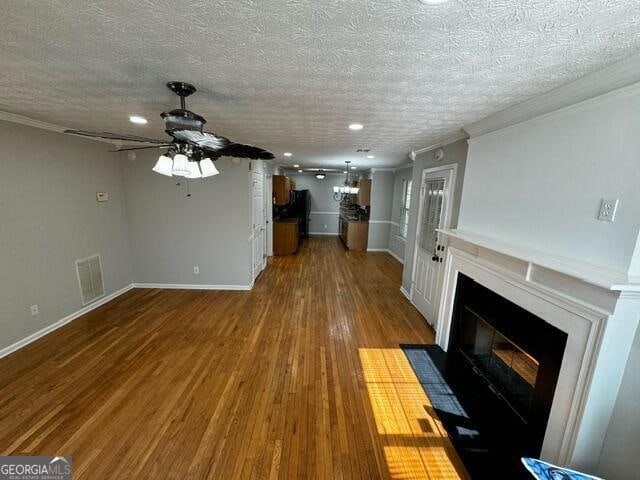 unfurnished living room featuring ceiling fan, ornamental molding, a textured ceiling, and hardwood / wood-style flooring