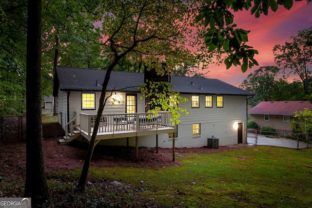 back house at dusk with a wooden deck and a lawn