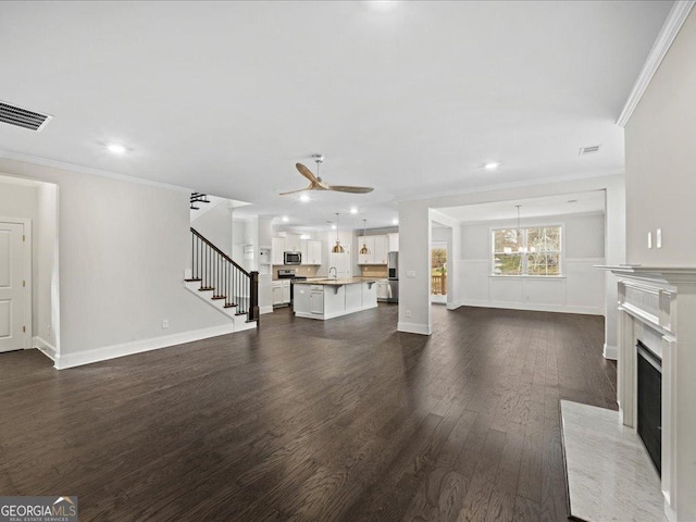 unfurnished living room featuring ceiling fan, sink, a high end fireplace, dark hardwood / wood-style floors, and ornamental molding