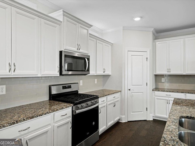 kitchen featuring appliances with stainless steel finishes, backsplash, dark stone countertops, dark hardwood / wood-style floors, and white cabinetry