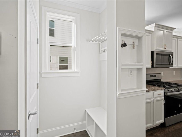 kitchen with appliances with stainless steel finishes, dark hardwood / wood-style flooring, dark stone counters, crown molding, and white cabinets