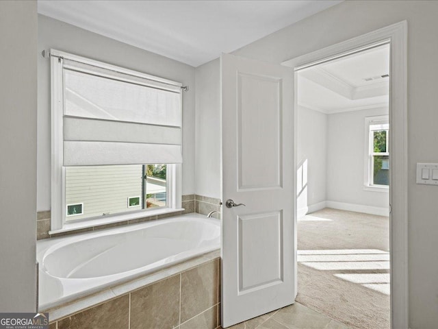 bathroom featuring a raised ceiling, crown molding, and tiled tub