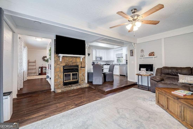 living room featuring hardwood / wood-style floors, a textured ceiling, a stone fireplace, and ceiling fan