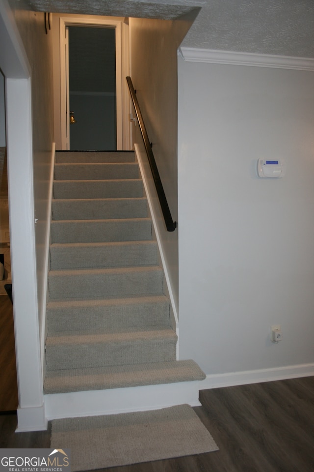 staircase with a textured ceiling, hardwood / wood-style flooring, and crown molding