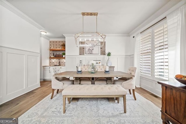 dining room with light hardwood / wood-style floors, crown molding, and an inviting chandelier