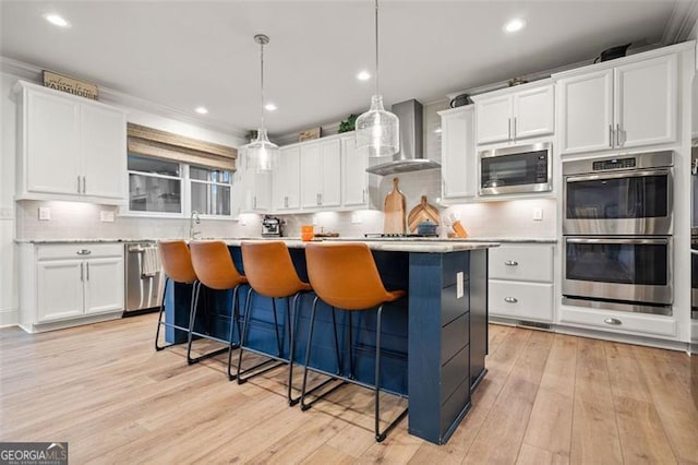 kitchen featuring white cabinetry, wall chimney exhaust hood, stainless steel appliances, decorative light fixtures, and a kitchen island