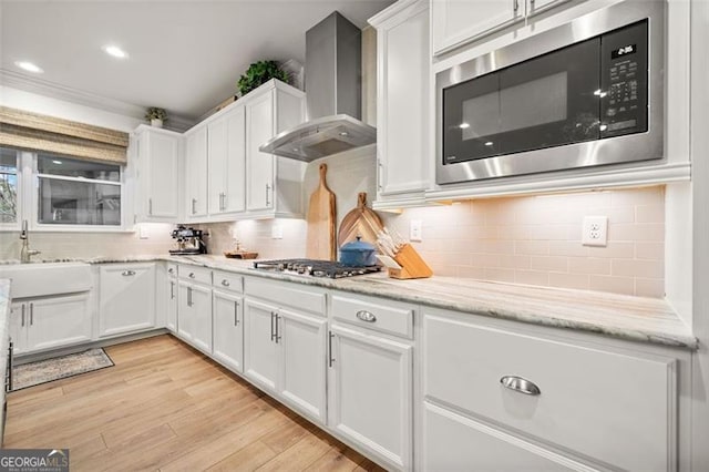 kitchen featuring backsplash, wall chimney range hood, light wood-type flooring, appliances with stainless steel finishes, and white cabinetry