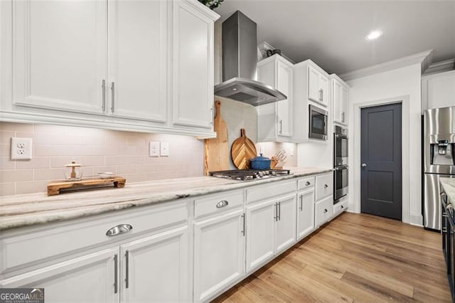 kitchen with wall chimney range hood, light hardwood / wood-style flooring, crown molding, white cabinets, and appliances with stainless steel finishes