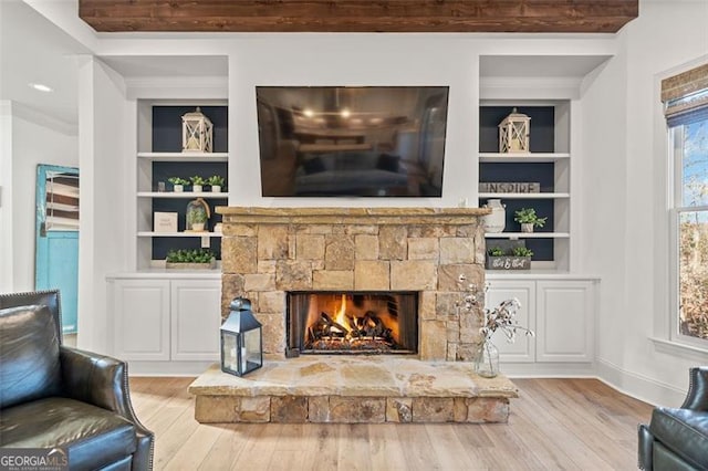 living room with a fireplace, built in shelves, light hardwood / wood-style floors, and ornamental molding