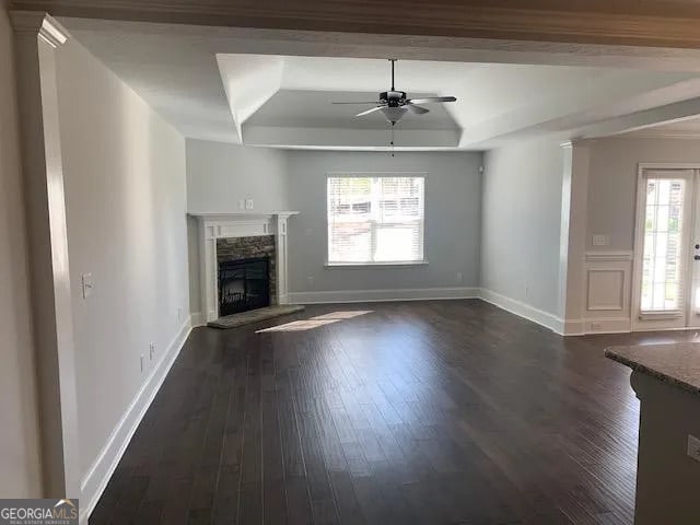 unfurnished living room featuring a raised ceiling, ceiling fan, dark hardwood / wood-style flooring, and a fireplace