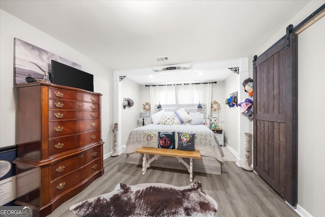 bedroom with a barn door and light hardwood / wood-style floors