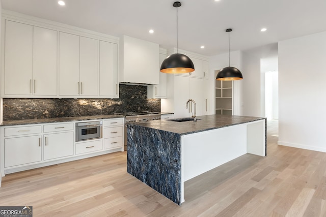 kitchen with sink, light hardwood / wood-style floors, white cabinetry, hanging light fixtures, and an island with sink