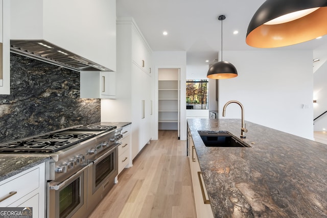 kitchen featuring white cabinetry, sink, wall chimney exhaust hood, pendant lighting, and range with two ovens