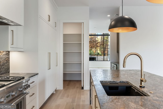 kitchen with white cabinetry, sink, high end stainless steel range oven, dark stone countertops, and light wood-type flooring