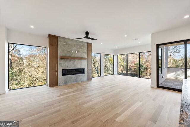 unfurnished living room with ceiling fan, a large fireplace, and light wood-type flooring