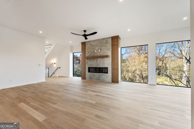 unfurnished living room featuring a large fireplace, ceiling fan, and light hardwood / wood-style flooring