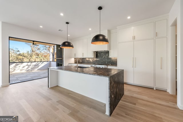 kitchen with white cabinetry, a center island with sink, pendant lighting, and light hardwood / wood-style floors